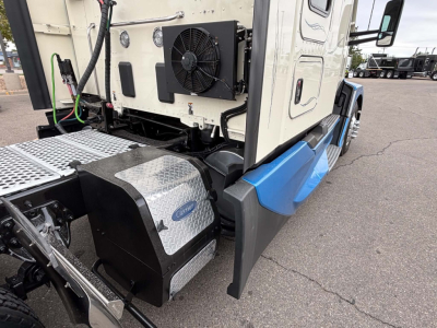 Kenworth T680 truck cab corner showing auxiliary coolant condenser and aluminum step plate with diamond plate texture near chassis.