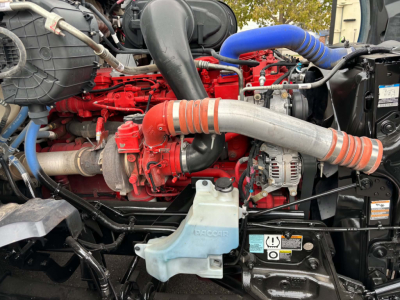 Kenworth T680 engine bay showing red engine block, blue coolant hose, gray radiator hoses, alternator, and coolant reservoir.