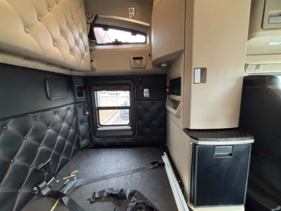 Kenworth T680 sleeper cab interior side view with quilted leather panels, window, and storage cabinet.