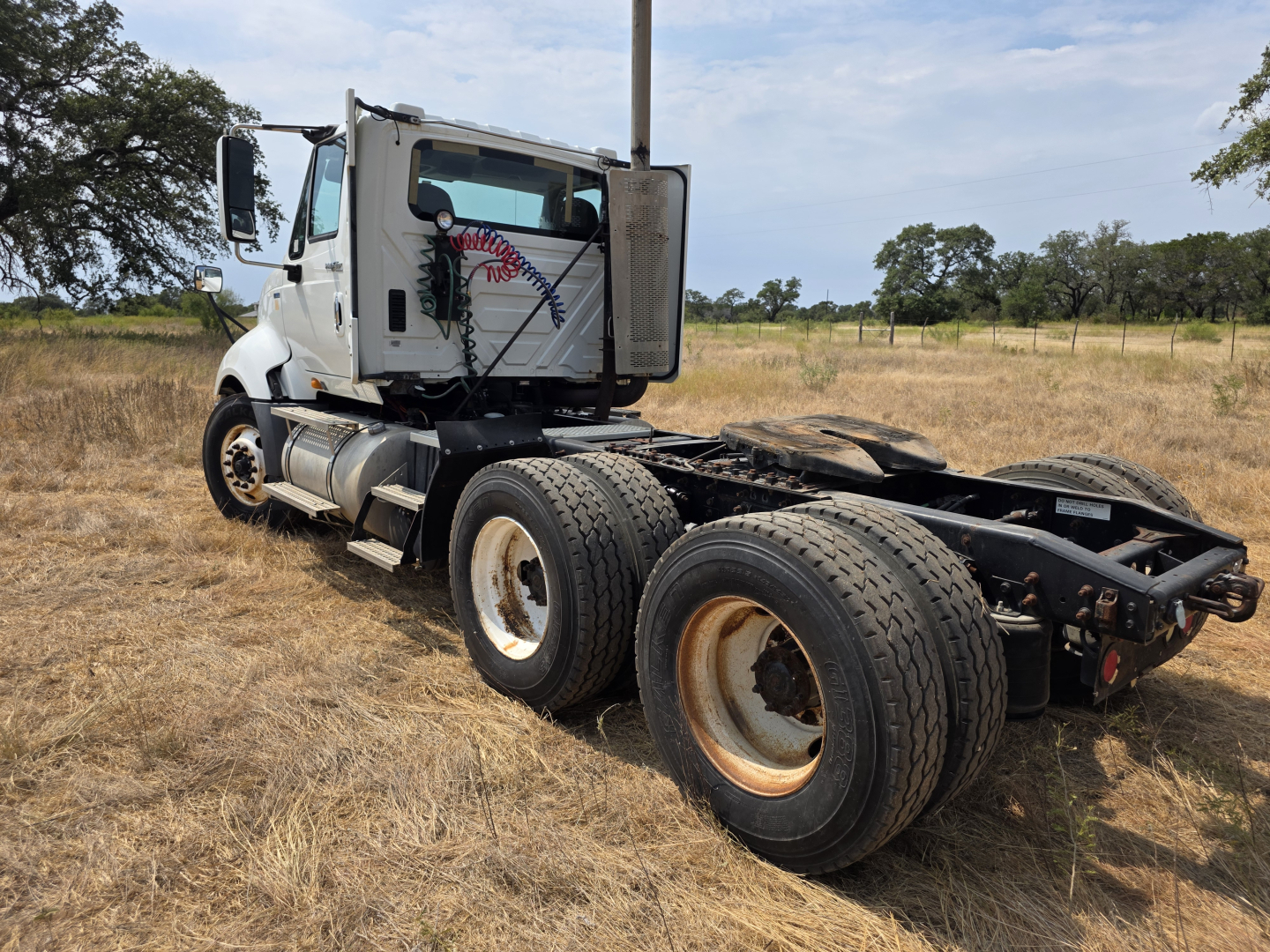 Truck chassis of a 2009 International Prostar day cab with dual rear axles and exposed cab, white cab with side logo, open field background.