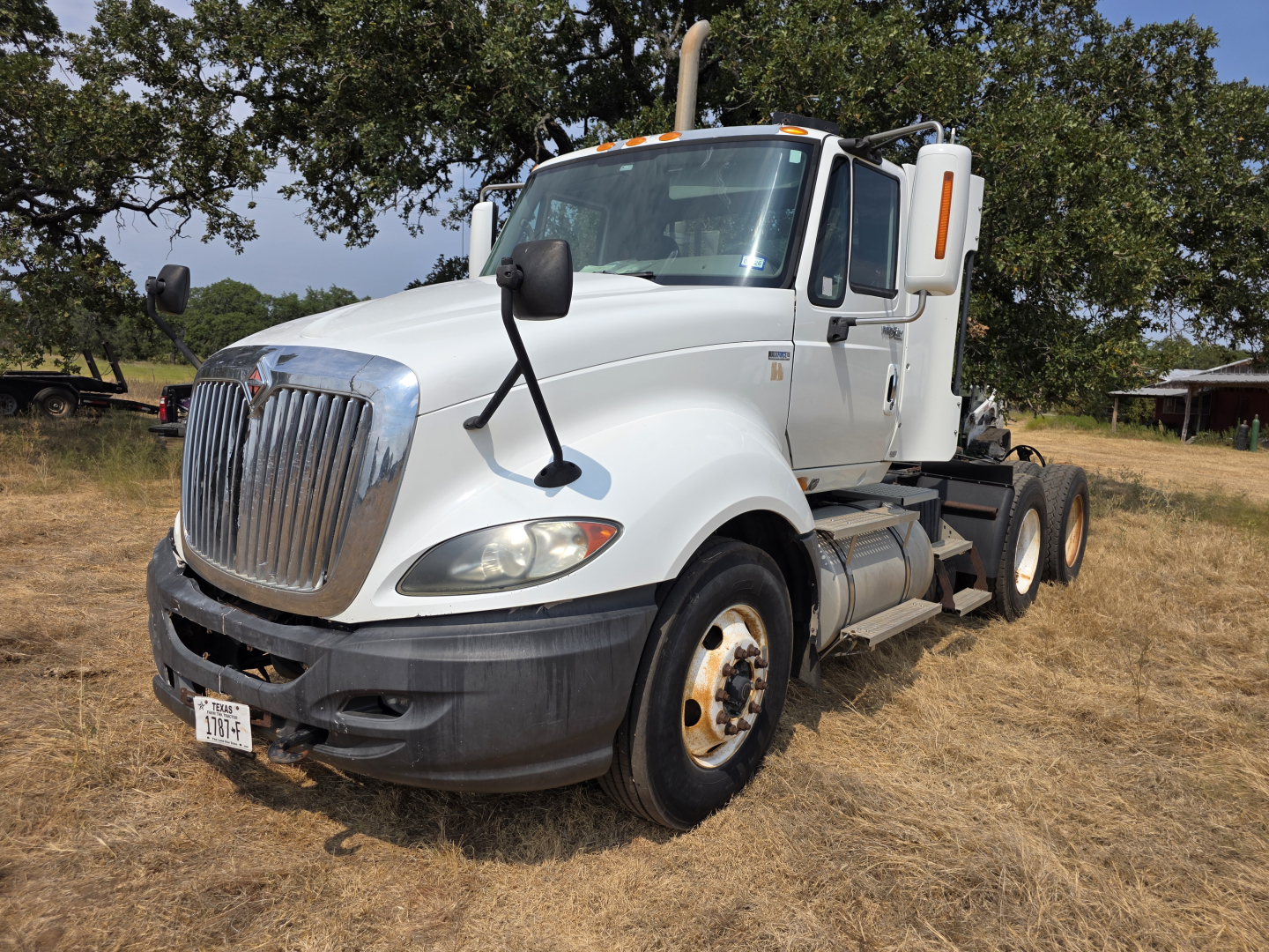 International Prostar day cab truck shown in a grassy lot with white cab, chrome grille, large side mirrors, and dual rear axles.