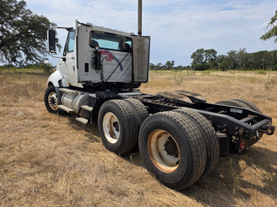 Truck chassis of a 2009 International Prostar day cab with dual rear axles and exposed cab, white cab with side logo, open field background.