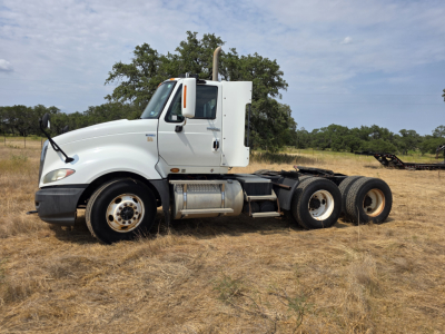 Truck side view showing 2009 International ProStar day cab with white cab, dual rear axles, and exposed fuel tank on dry field.