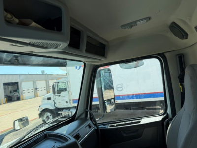Cab interior of a Volvo VNR truck showing overhead storage compartments and a side window with a view of other trucks outside.