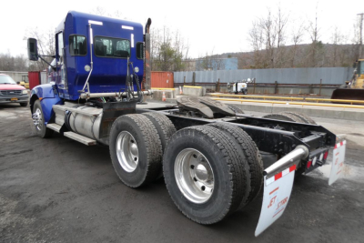 Kenworth T660 conventional daycab semi-truck chassis with blue cab and dual rear axles, rear view showing fuel tanks and mud flaps.