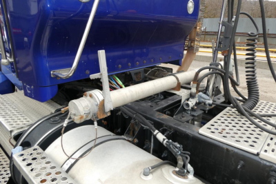 Truck chassis showing hydraulic lines and fuel/tank components under blue Kenworth cab side view.