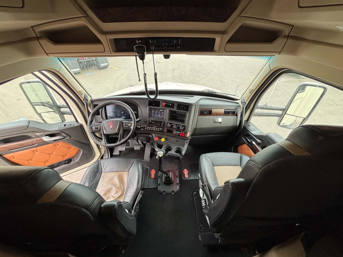 Kenworth T680 cabin interior showing steering wheel, dashboard, and front seats with controls and sunroof, view from rear cabin.