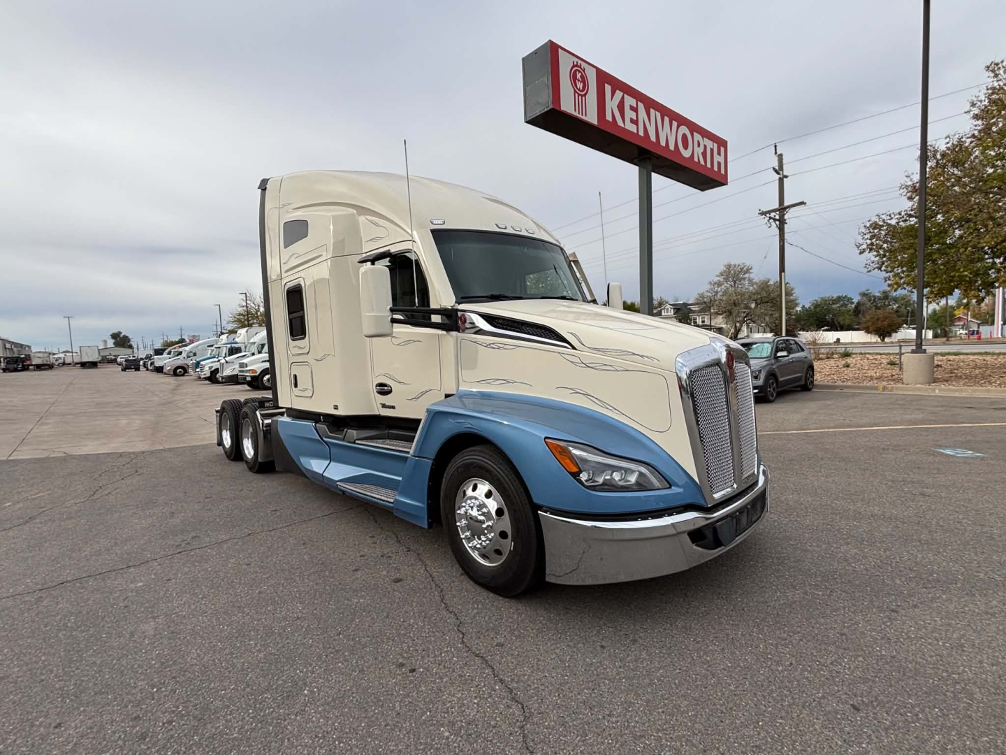 Kenworth T680 day cab tractor in two-tone white and blue with Kenworth sign in background.