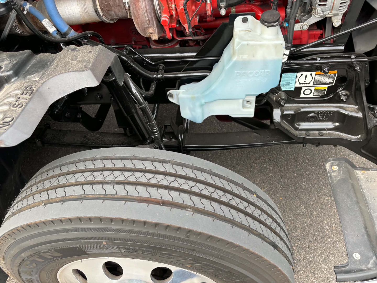 Kenworth T680 engine bay with coolant reservoir and front wheel. Visible labels and hoses in view.