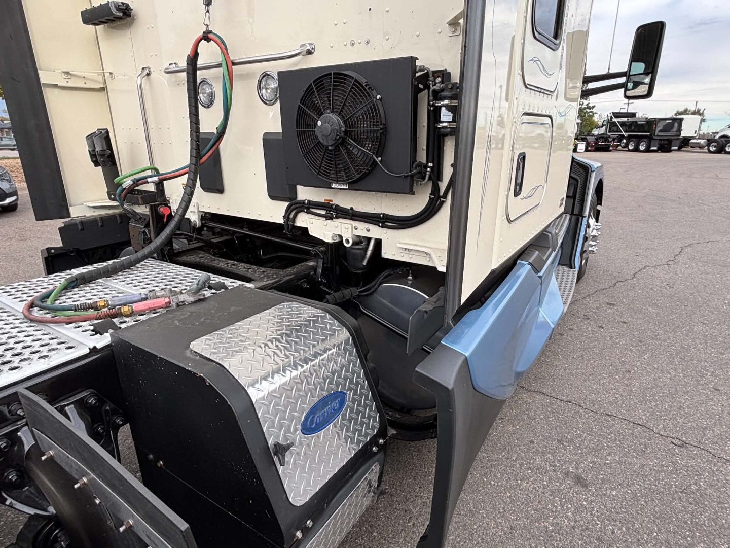 Kenworth T680 side engine bay area showing auxiliary radiator and coolant lines mounted near the cab with diamond plate toolbox and steps.