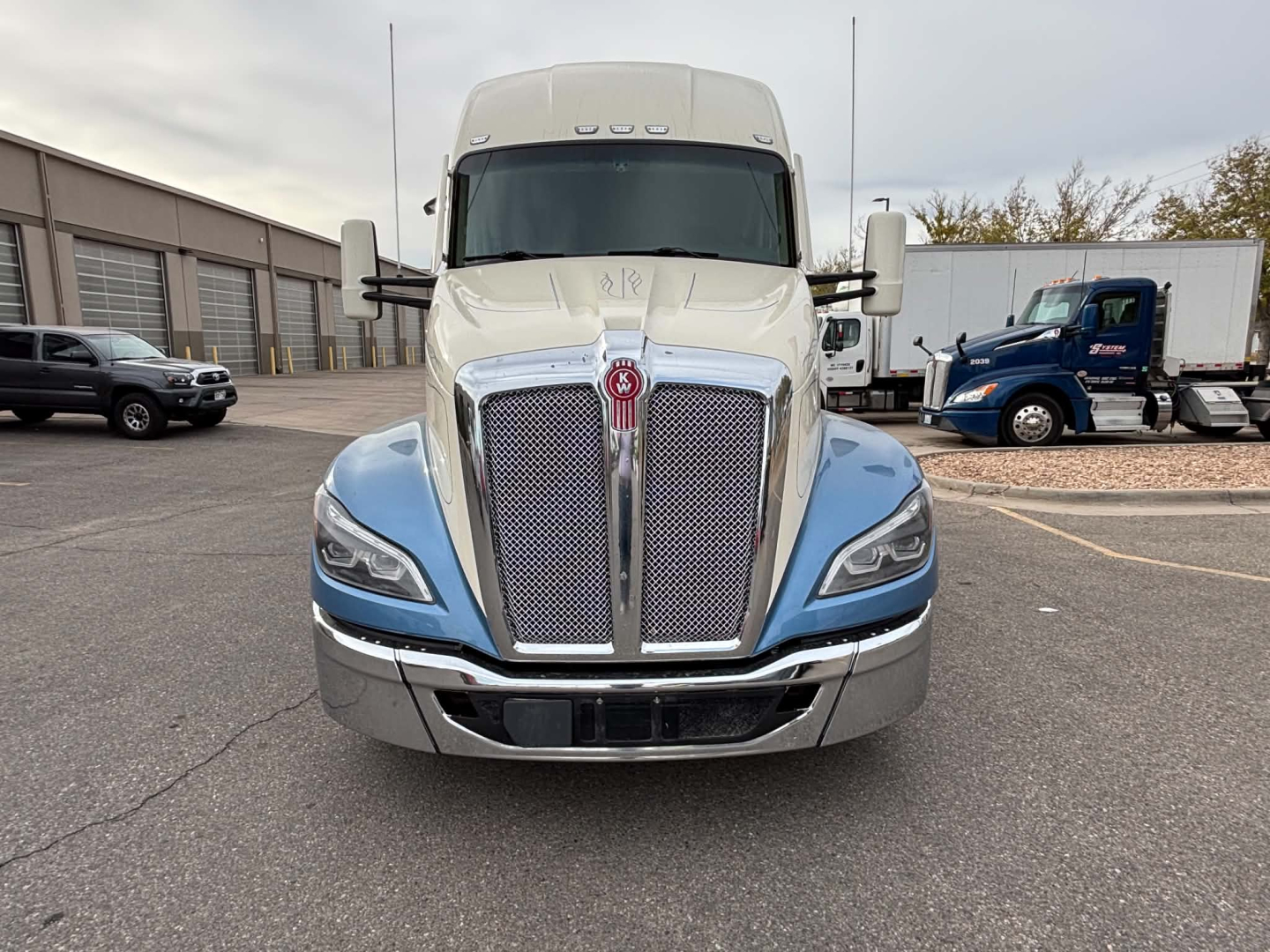 Kenworth T680 front view with two-tone blue and beige cab, chrome grille, large bumper, and KW emblem.