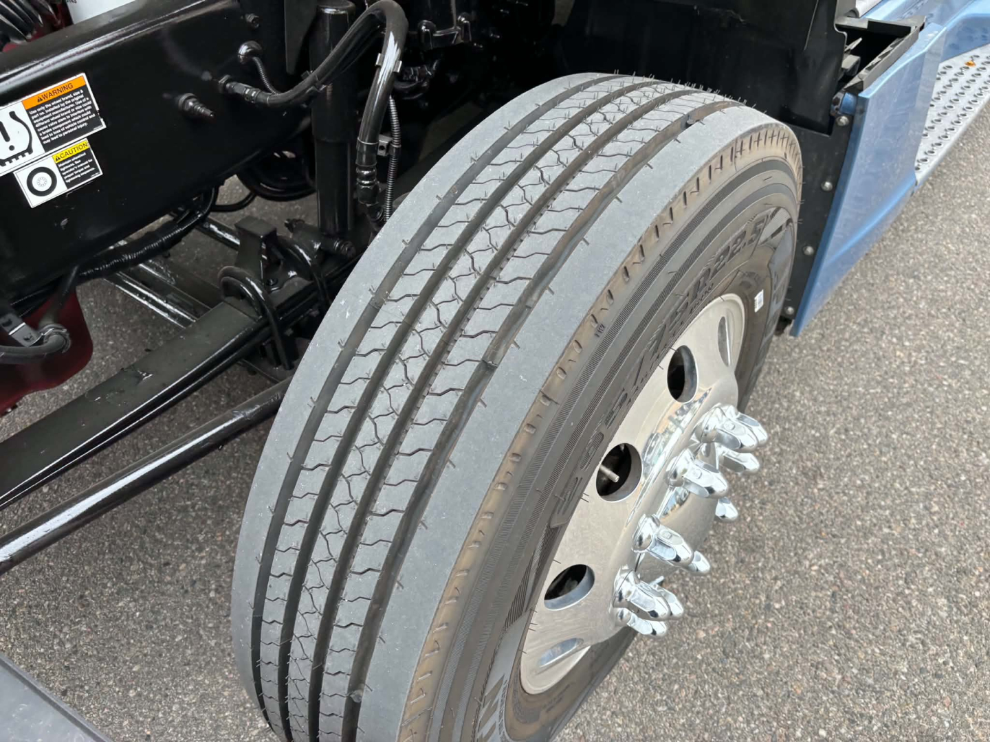 Kenworth T680 front wheel showing dual tires and hub with lug nuts, undercarriage and frame visible.