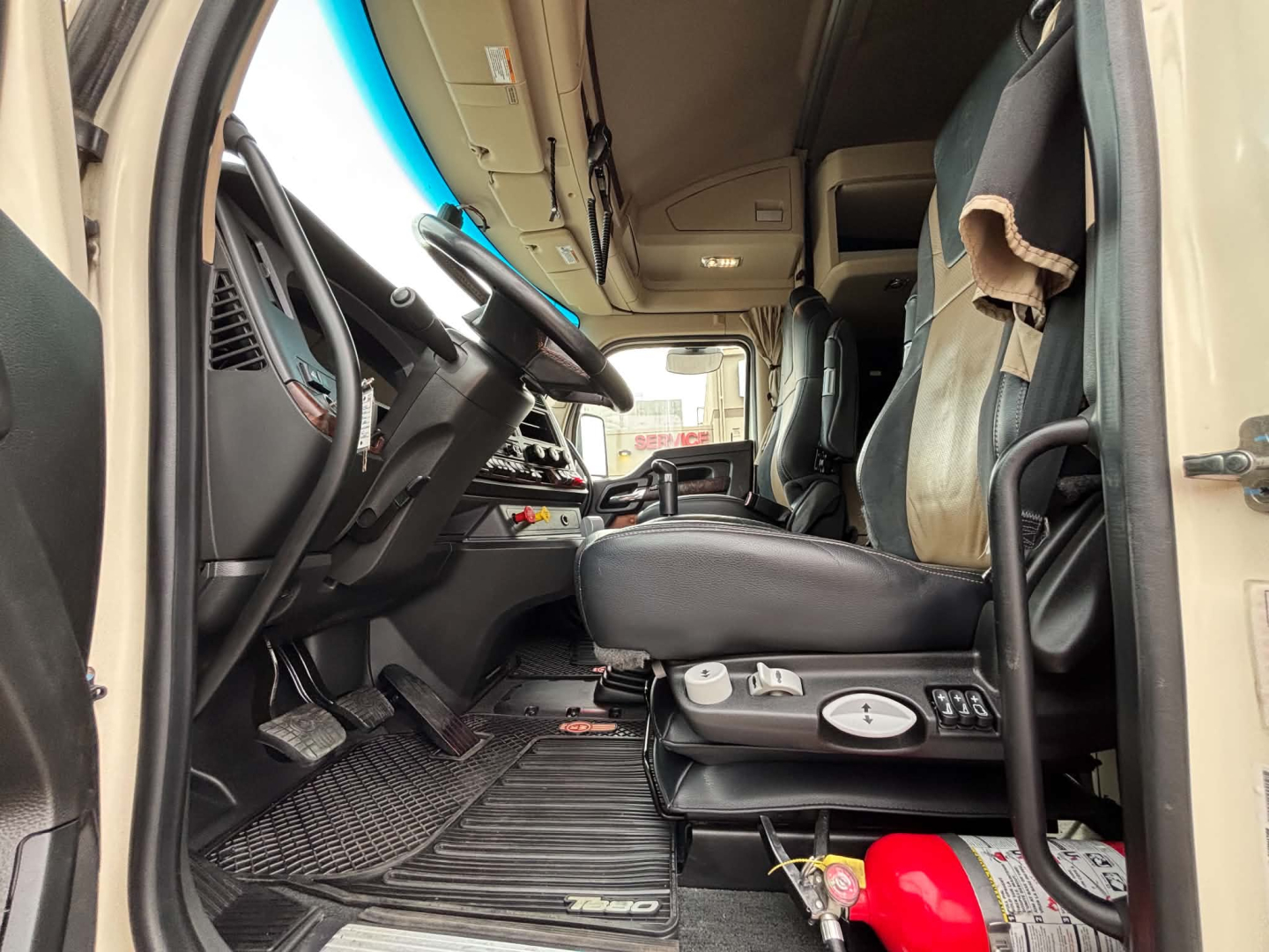 Kenworth T680 interior driver seat and dashboard view showing steering wheel, pedals, and center console with controls.