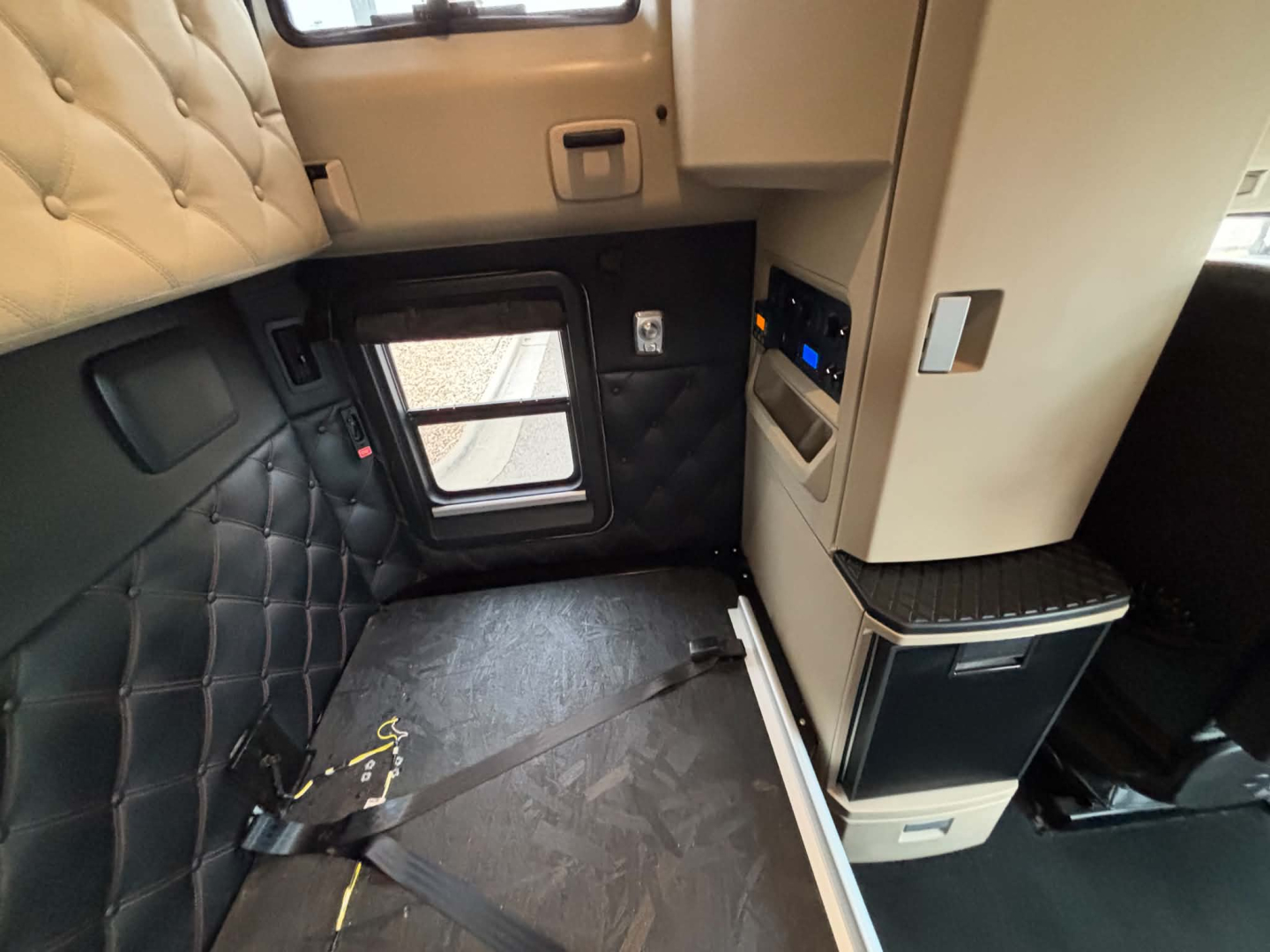 Kenworth T680 interior sleeper cab area with quilted door panel and window, storage compartments, and control panel visible.