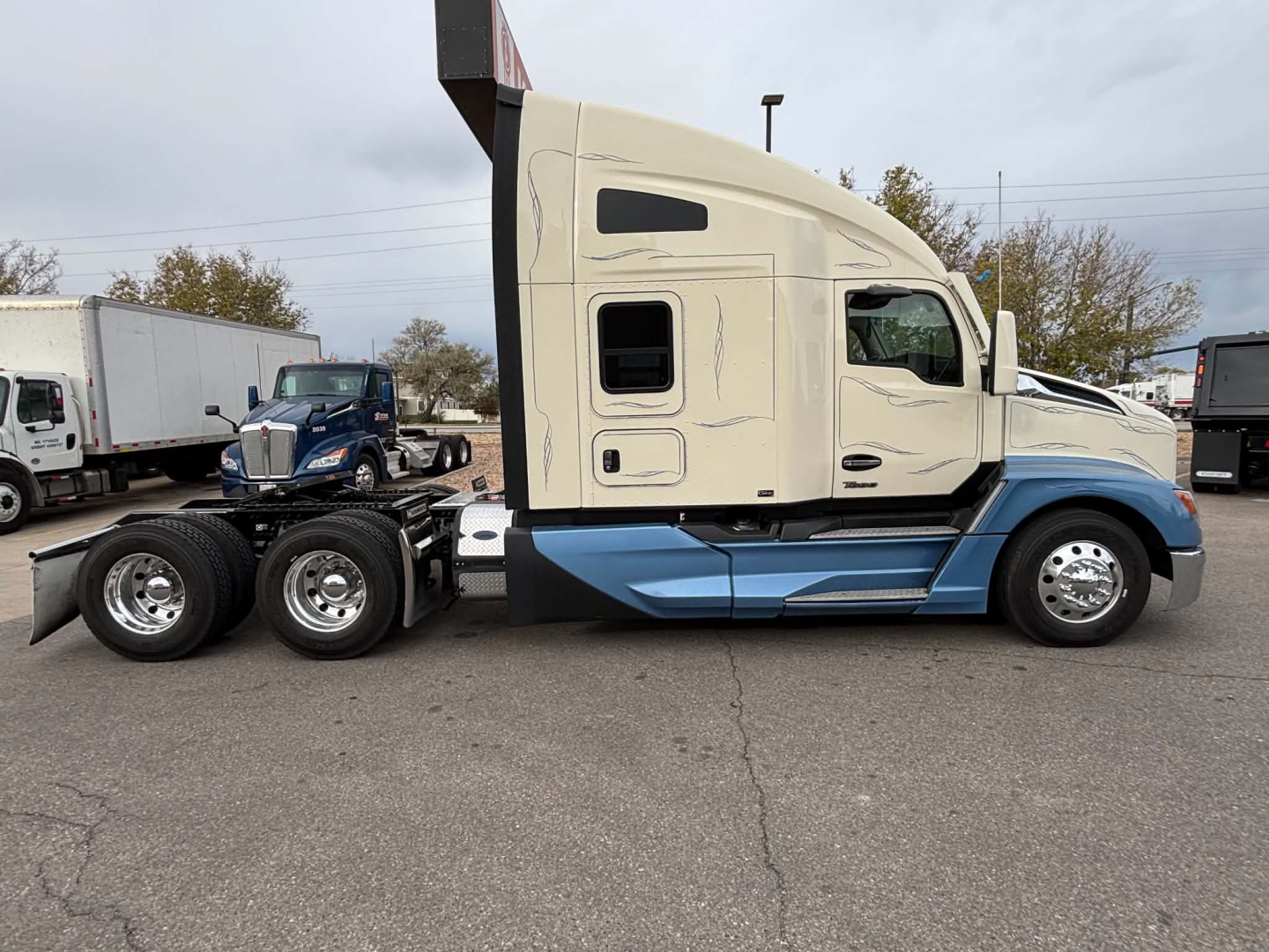 Kenworth T680 tractor truck side view showing sleeper cab and blue lower accent with beige upper cab.
