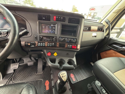 Dashboard of a Kenworth T680 interior showing steering wheel, center console with touchscreen display, climate controls, gear shifter, and pedal cluster.
