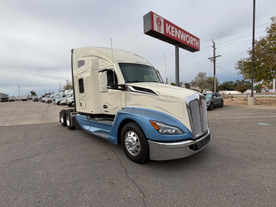 Kenworth T680 day cab tractor in two-tone white and blue with Kenworth sign in background.