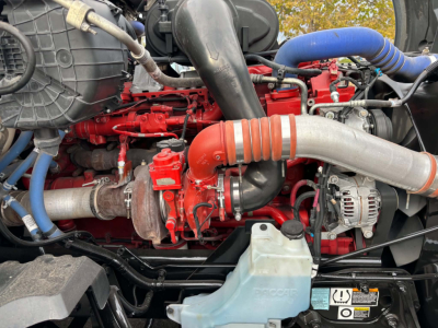 Kenworth T680 engine bay showing red engine components, large intake hose, blue coolant hose, alternator, and various hoses and wiring.