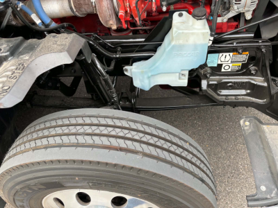 Kenworth T680 engine bay with coolant reservoir and front wheel. Visible labels and hoses in view.