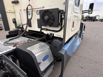 Kenworth T680 side engine bay area showing auxiliary radiator and coolant lines mounted near the cab with diamond plate toolbox and steps.