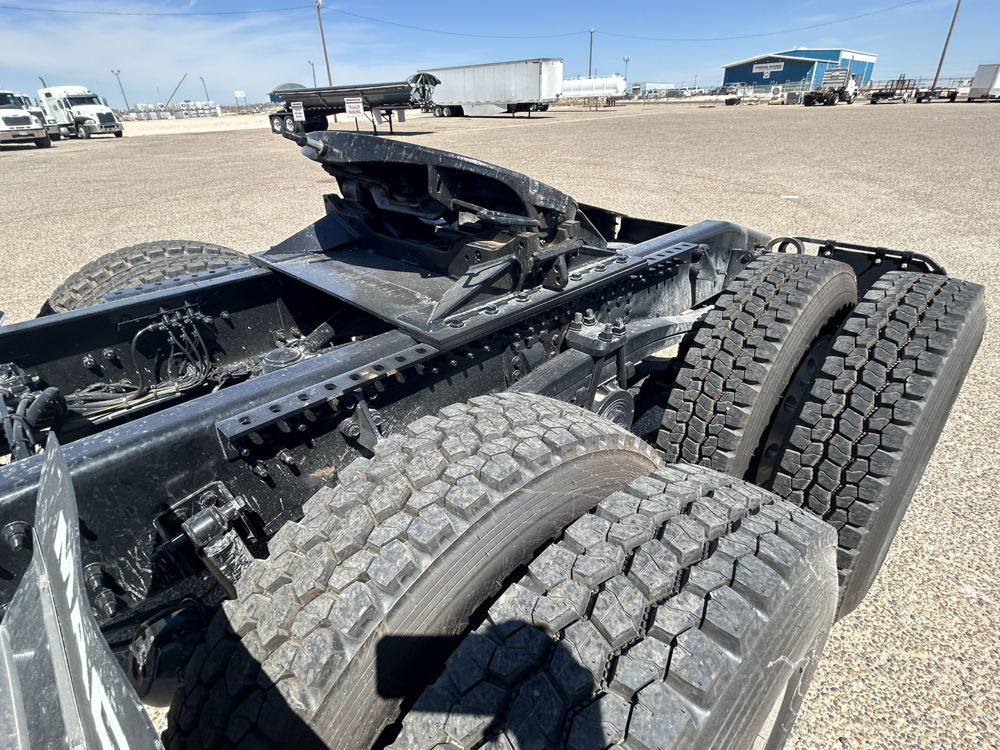Chassis view of a Mack GR64FT truck frame showing dual rear axles and heavy-duty tires with fifth wheel and undercarriage components visible.