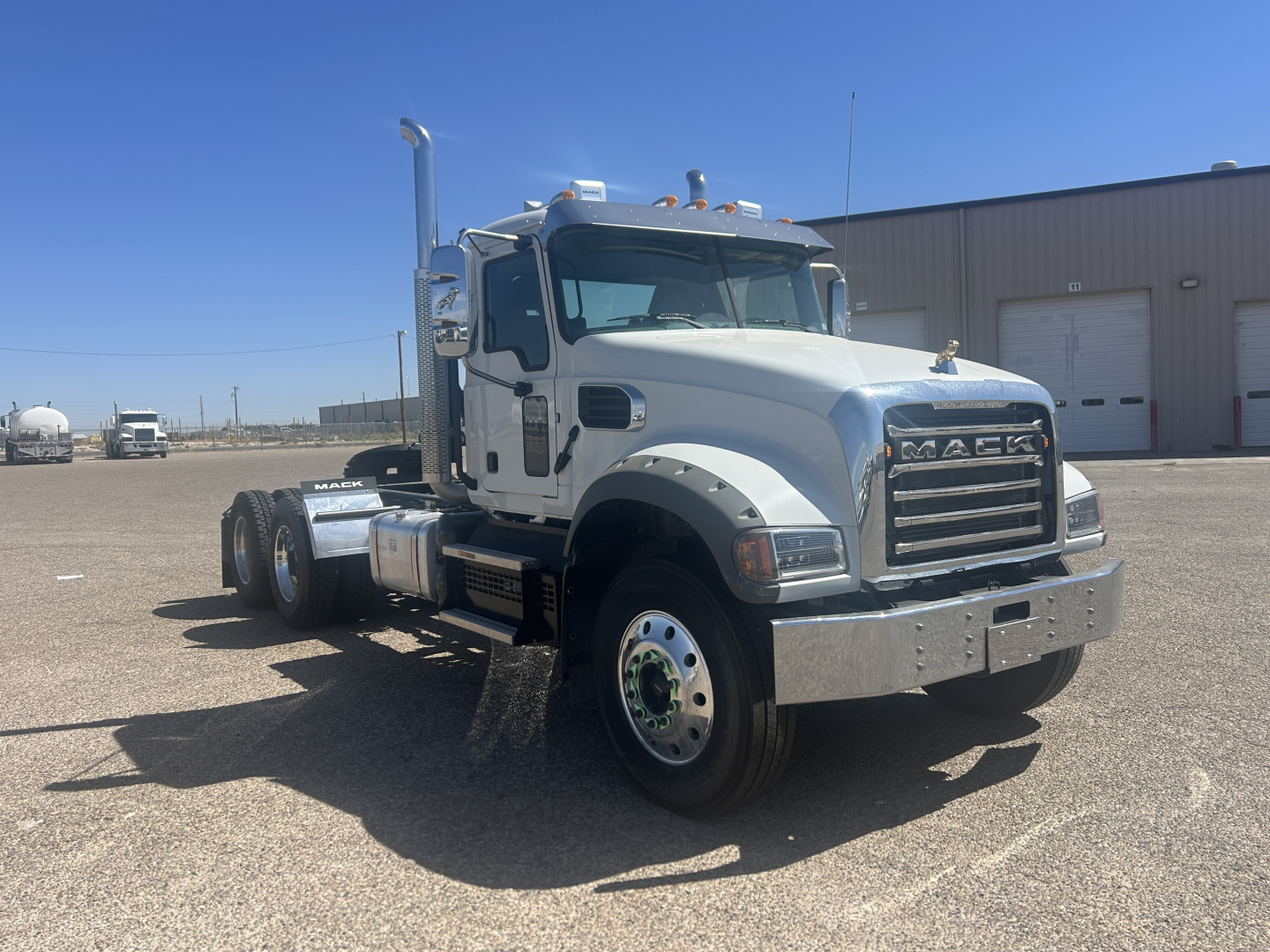 Mack GR64FT conventional daycab truck shown in a parking lot, front-left angle with chrome bumper, large grille, dual rear axles, front tire, and side exhaust.