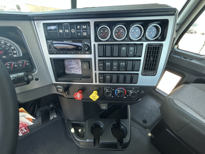 Dashboard of a new 2027 Mack GR64FT day cab showing gauges, gear selector, switches, and control panel with two cup holders below.