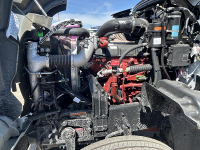 Truck engine bay with various hoses, wiring, and components; red engine block center; labels and caps visible.
