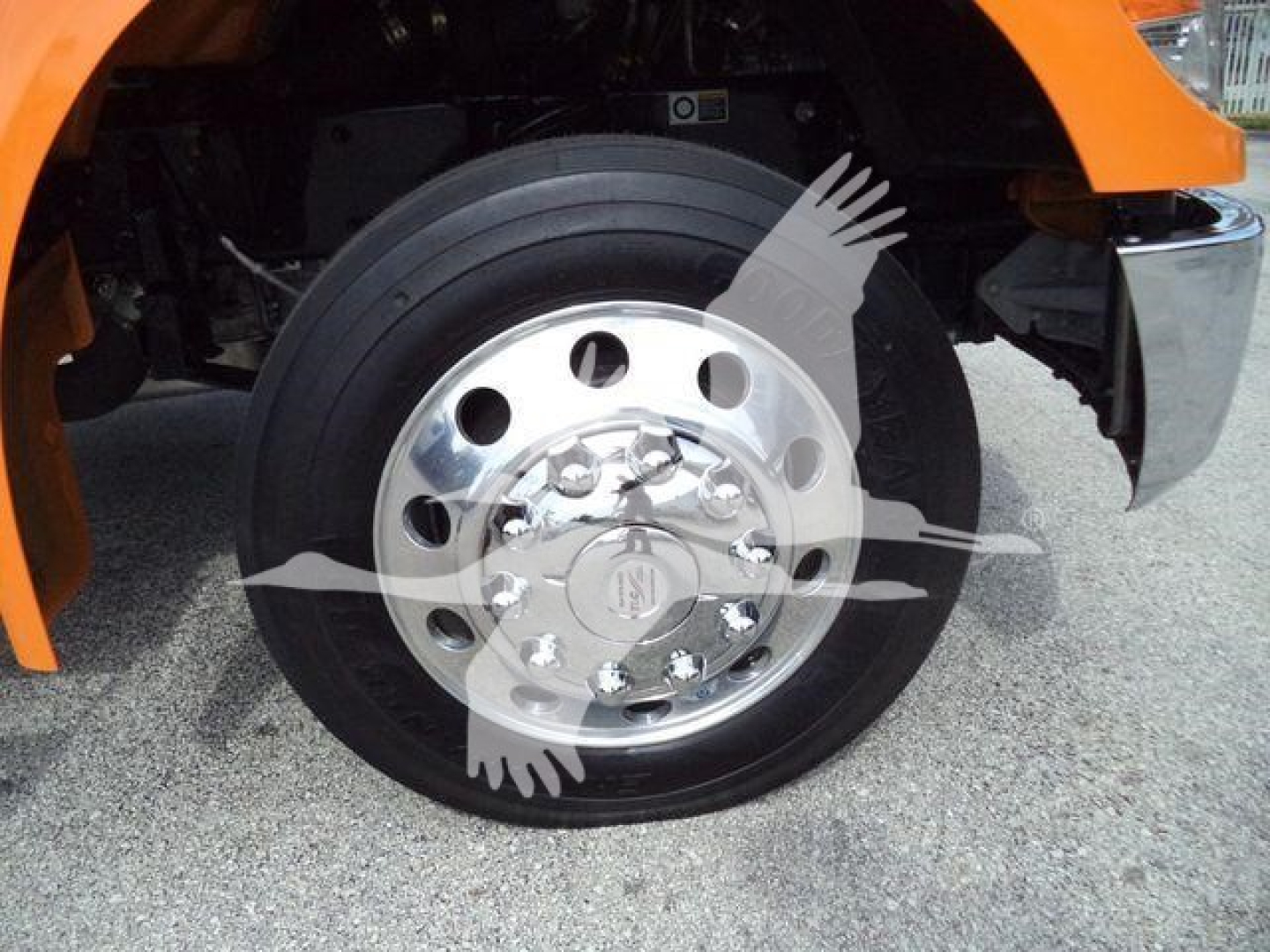 Kenworth T280 front wheel showing aluminum chrome wheel and tire, part of orange cab visible in fender area.