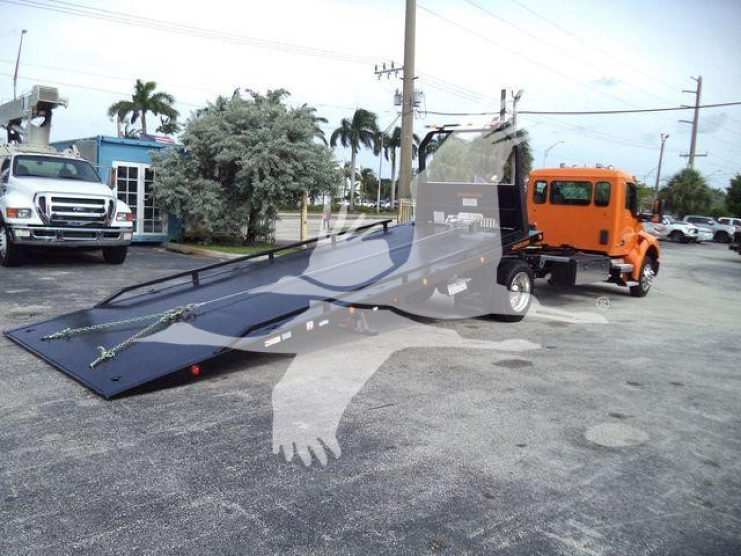 Orange Kenworth rollback tow truck with extended flatbed trailer in a parking lot.
