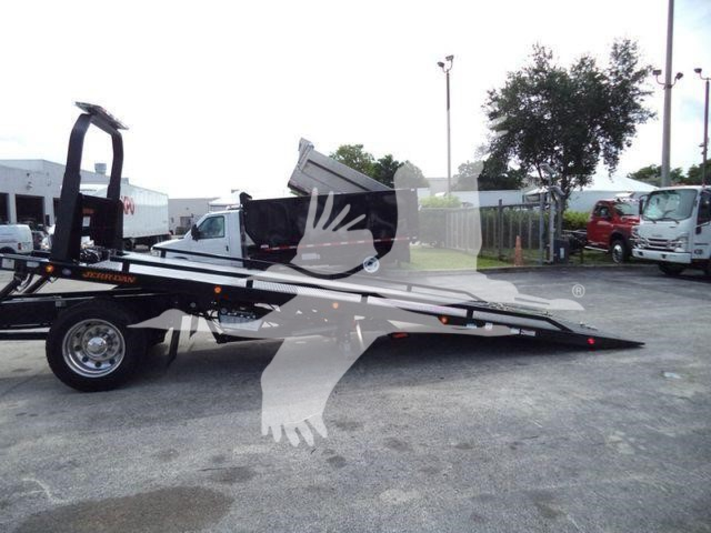 Kenworth rollback tow truck flatbed with orange accent, loading ramps extended, side view. Visible text includes 'KENWORTH' on chassis and 'ROLLBACK' on equipment.