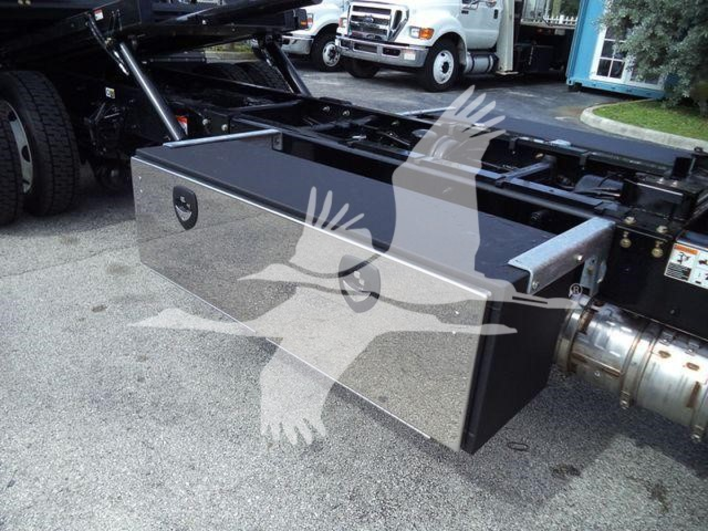 Kenworth T280 rollback chassis with a large rectangular tool/storage box mounted under the frame; chrome polished lid and black sides visible.