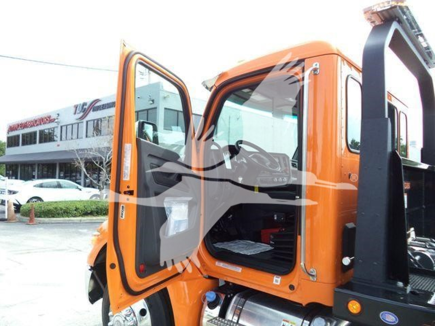 Truck cab exterior with open orange doors showing the cabin interior and step seating, Kenworth T-series style, rollback equipment attached.