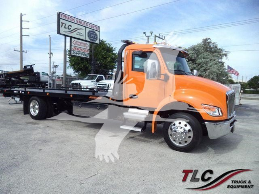 Kenworth T280 rollback tow truck with orange cab and flatbed, TLC Truck Sales Center logo visible, slight reflection on window