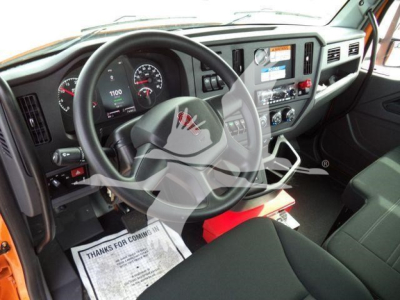 Truck cab interior view of a 2025 Kenworth T280 with steering wheel, dashboard gauges, center console, and orange exterior trim visible from the driver's seat.