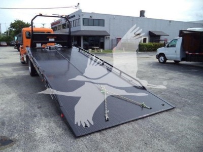 Kenworth T280 rollback tow truck with long flatbed viewed from rear-left, orange cab in background, loading surface with chains