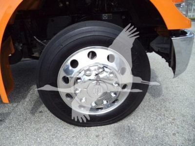 Kenworth T280 front wheel showing aluminum chrome wheel and tire, part of orange cab visible in fender area.