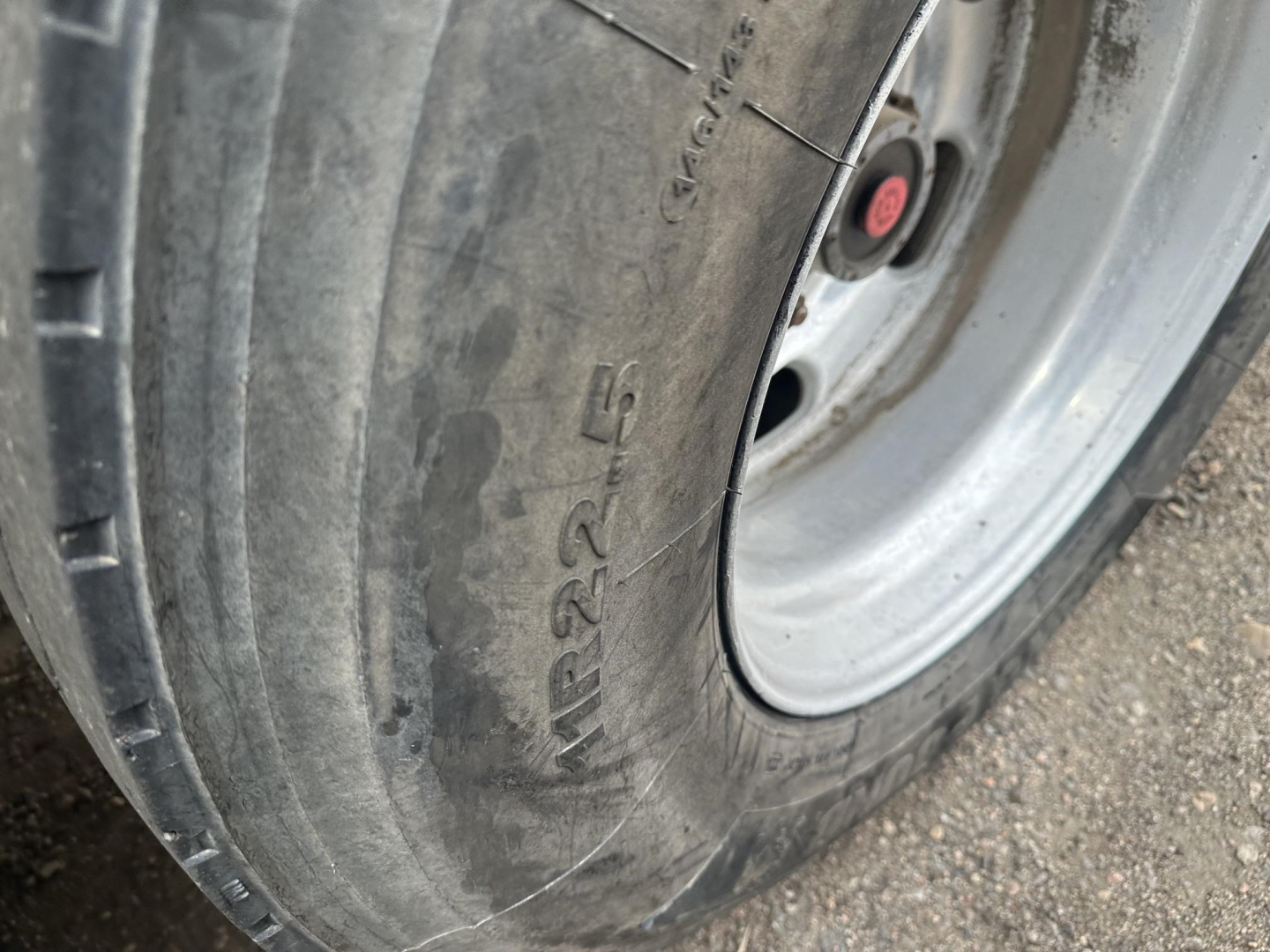 Tire and wheel close-up on frameless aluminum end dump trailer showing tire tread and wheel hub; visible markings on tire include 'MR22-5' and other molded text.