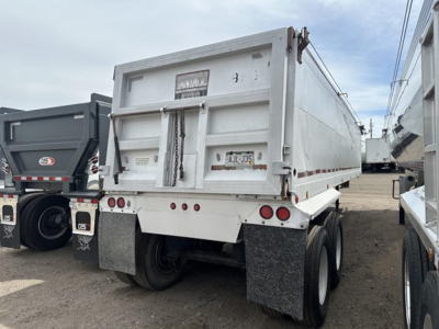 Dump trailer showing frameless aluminum end dump with rear doors and dual axle setup. License plate and mud flaps visible; white color and reflective tape along sides.