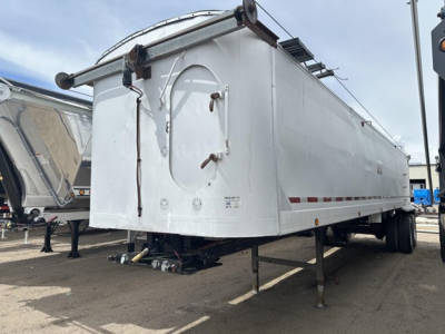 Frameless aluminum end dump trailer viewed from side/front showing landing gear and underside. Text and decals faint on sides; hydraulic components and hitch visible.