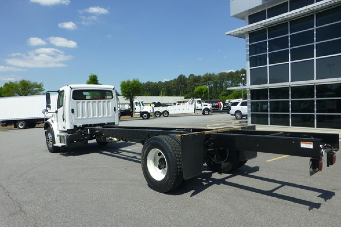 Freightliner M2 106 Plus cab chassis with flatbed rail, front truck cab and long chassis frame in a dealership lot.