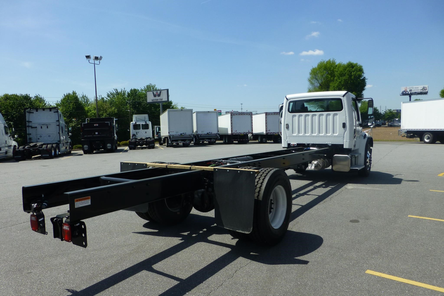 Chassis cab of a Freightliner M2 106 Plus (2027) showing the black frame rail and rear dual wheels with cab at front, VIN 1FVACWFC4VHWX8828 visible in listing context.