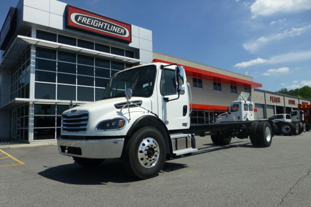 Freightliner M2 106 Plus cab and chassis truck in front of dealership building showing white cab and chassis with Freightliner logo.