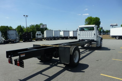 Freightliner M2 106 cab and chassis rear view showing frame rails and dual rear wheels with white cab in background.