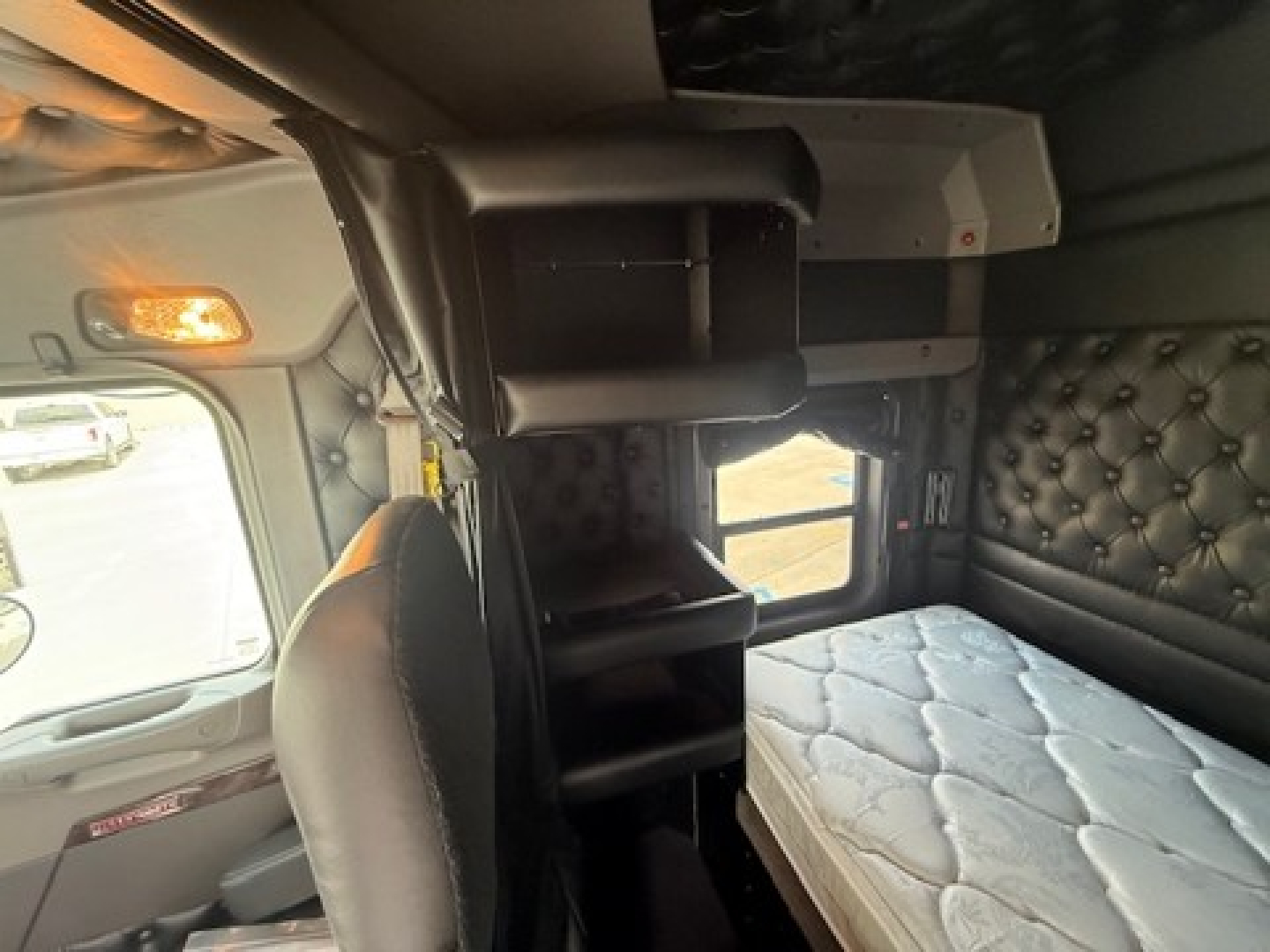 Cab interior of a Kenworth W900L sleeper with bunk area, overhead storage, quilted door panels, and a visible bed mattress.