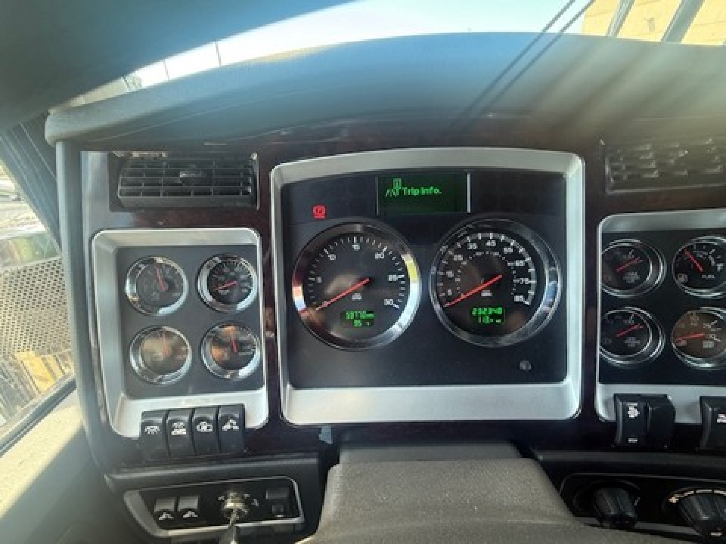 Kenworth W900L dash showing gauge cluster and instrument panel with multiple switches and vents.