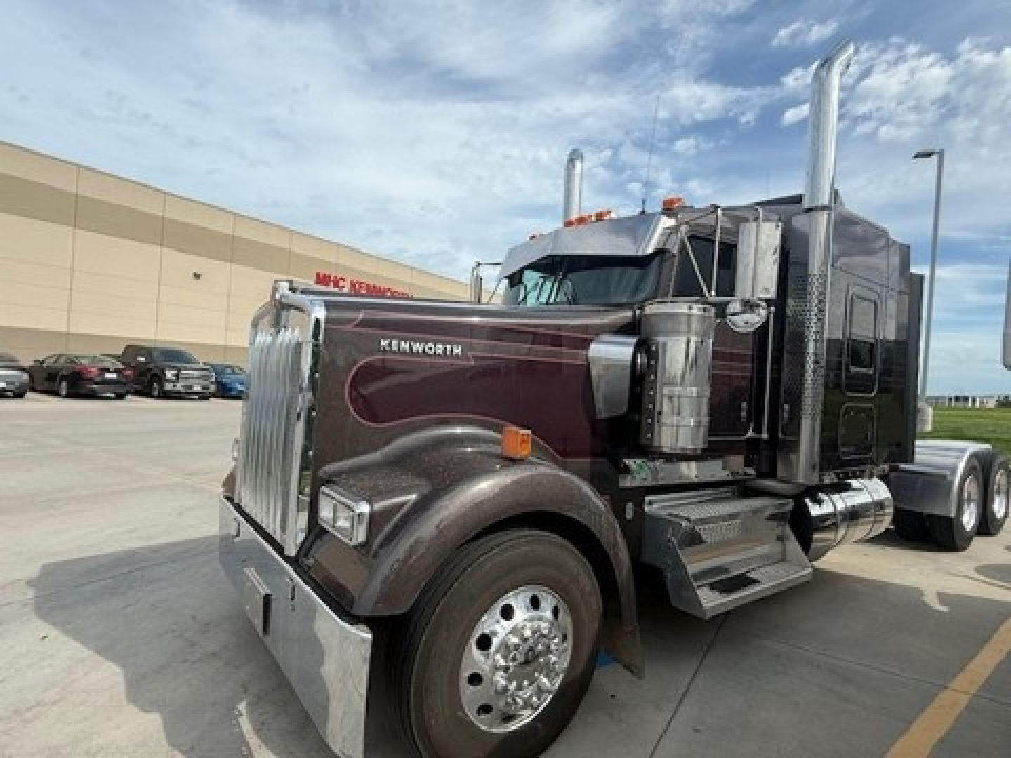Kenworth W900L conventional sleeper truck side view showing chrome exhaust stacks and maroon/black tractor with chrome grille and fuel tanks.