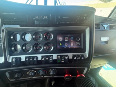 Truck dashboard and center console with multiple gauges, a touchscreen infotainment display, and control switches; Kenworth branding on the dash.