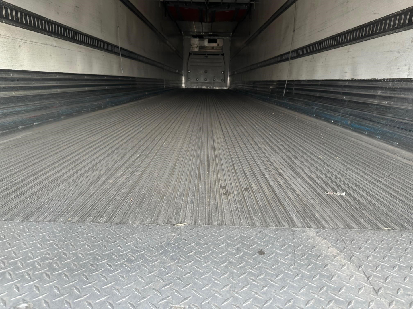 trailer interior with ribbed metal floor and sidewalls, empty reefer trailer with rear door opening visible