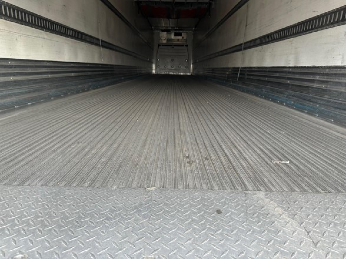 Great Dane reefer trailer interior showing ribbed metal floor and sidewalls; empty cargo space with rear doors in distant view.